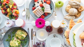 Un desayuno con una variedad de platillos, incluyendo waffles, fruta, pasteles y huevos Benedict.
