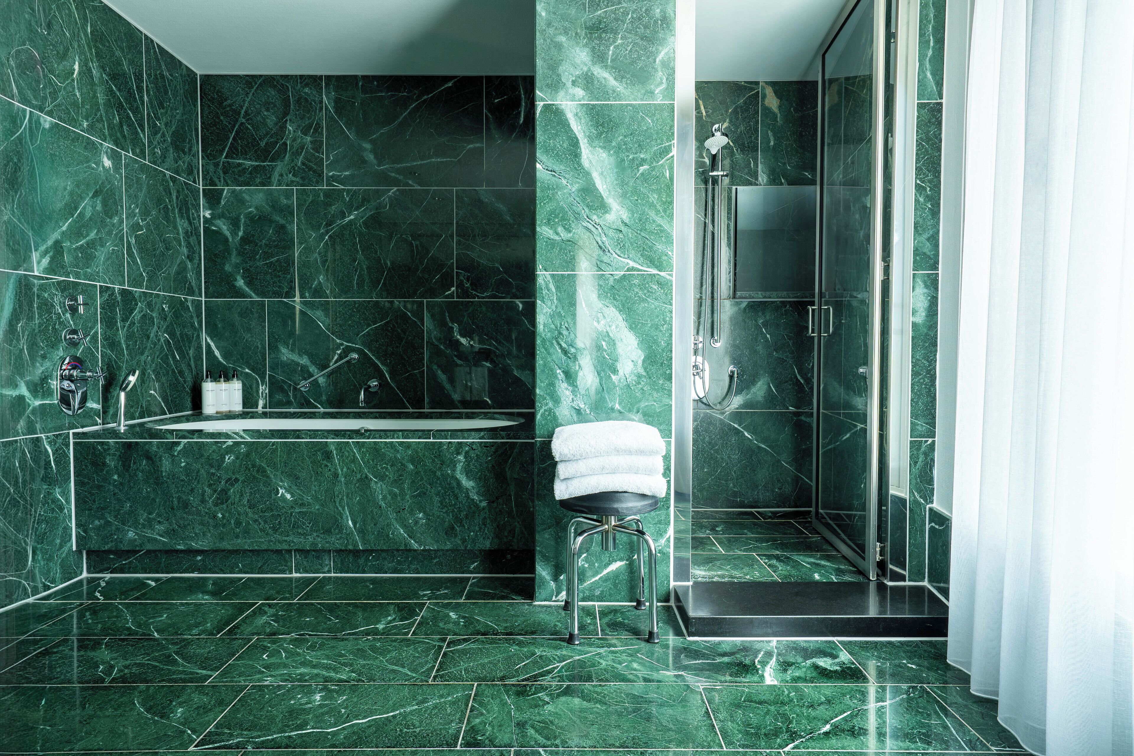 Ein modernes Badezimmer mit Marmorboden und -wänden, einer Glasdusche und einem kleinen Hocker mit Handtuch.