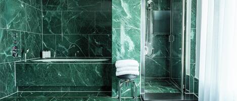A modern bathroom with a marble floor and walls, a glass shower enclosure, and a small stool with a towel.