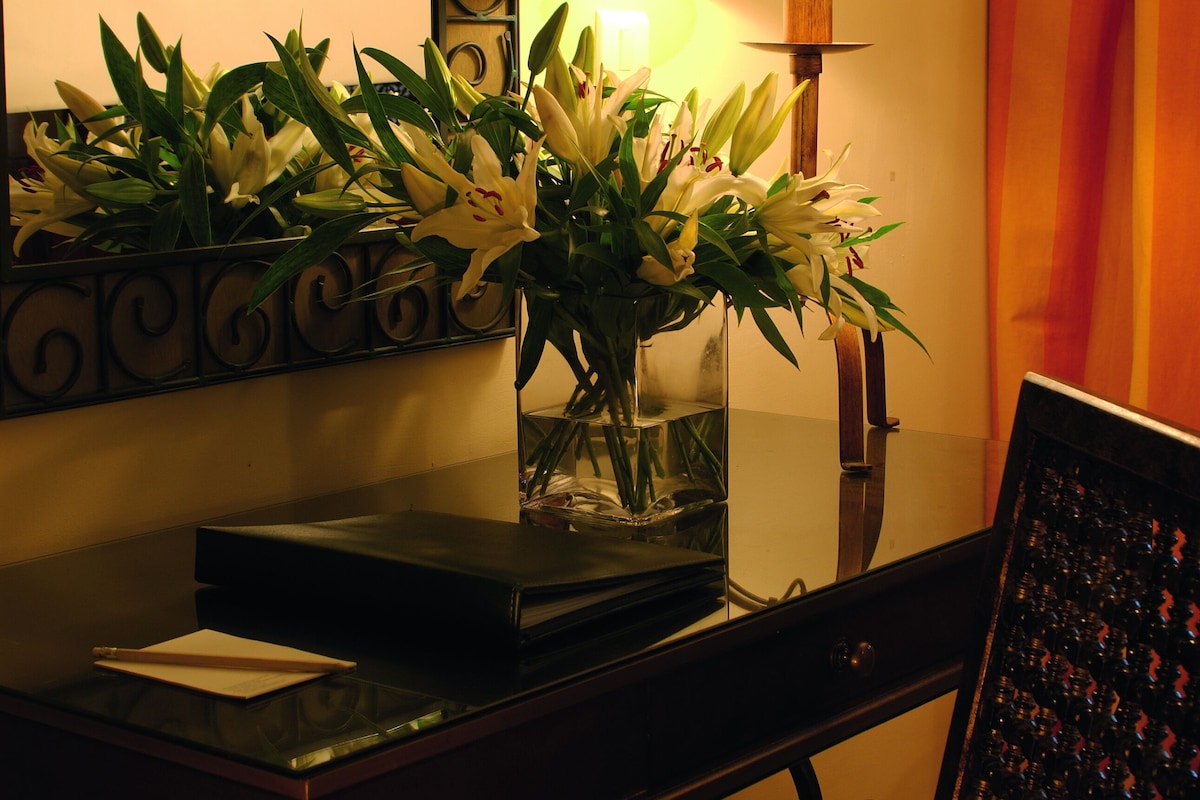 A desk with a vase of flowers, a lamp, and a framed picture.