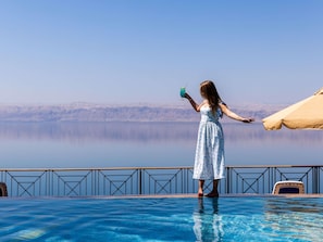 Una persona está junto a una piscina, con una vista despejada de un paisaje montañoso al fondo.