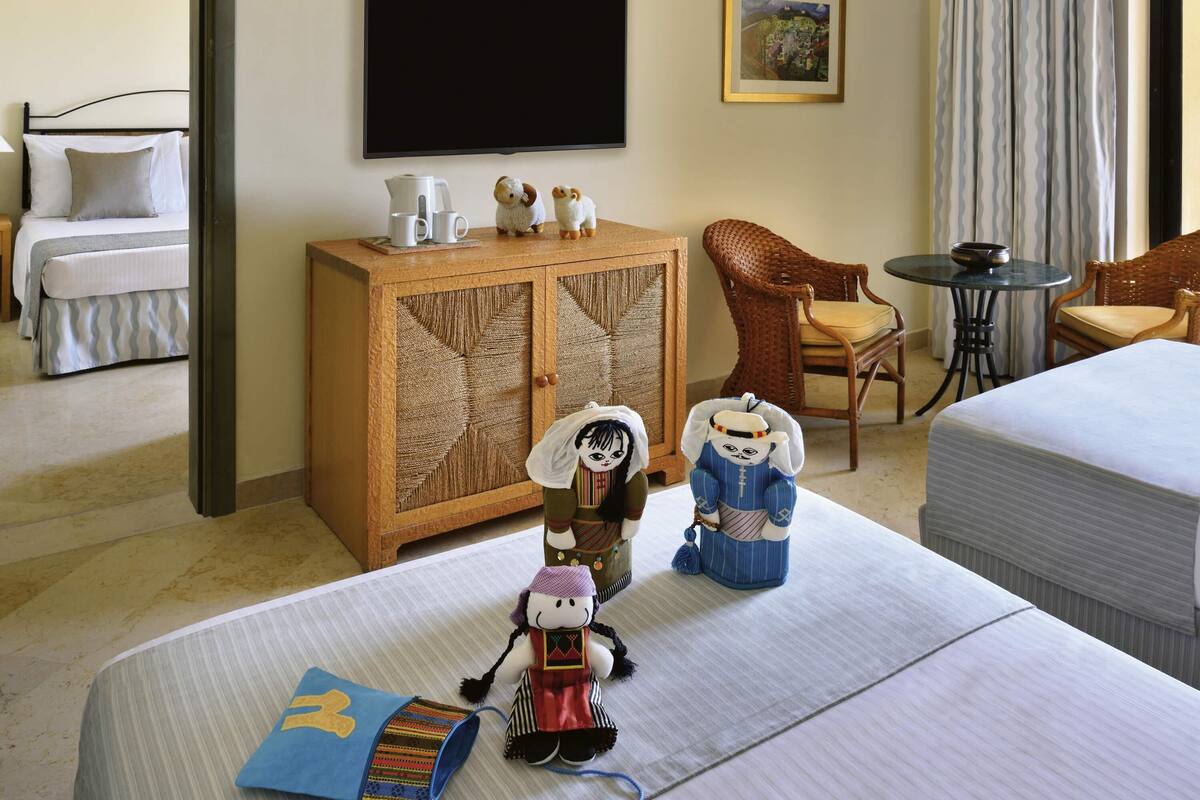 A hotel room with a bed, a wooden cabinet, a television, a painting, and a dining area with chairs and a table.