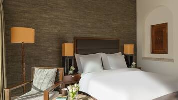 Una habitación de hotel con una cama grande, una silla de madera, una mesita redonda pequeña y una lámpara.