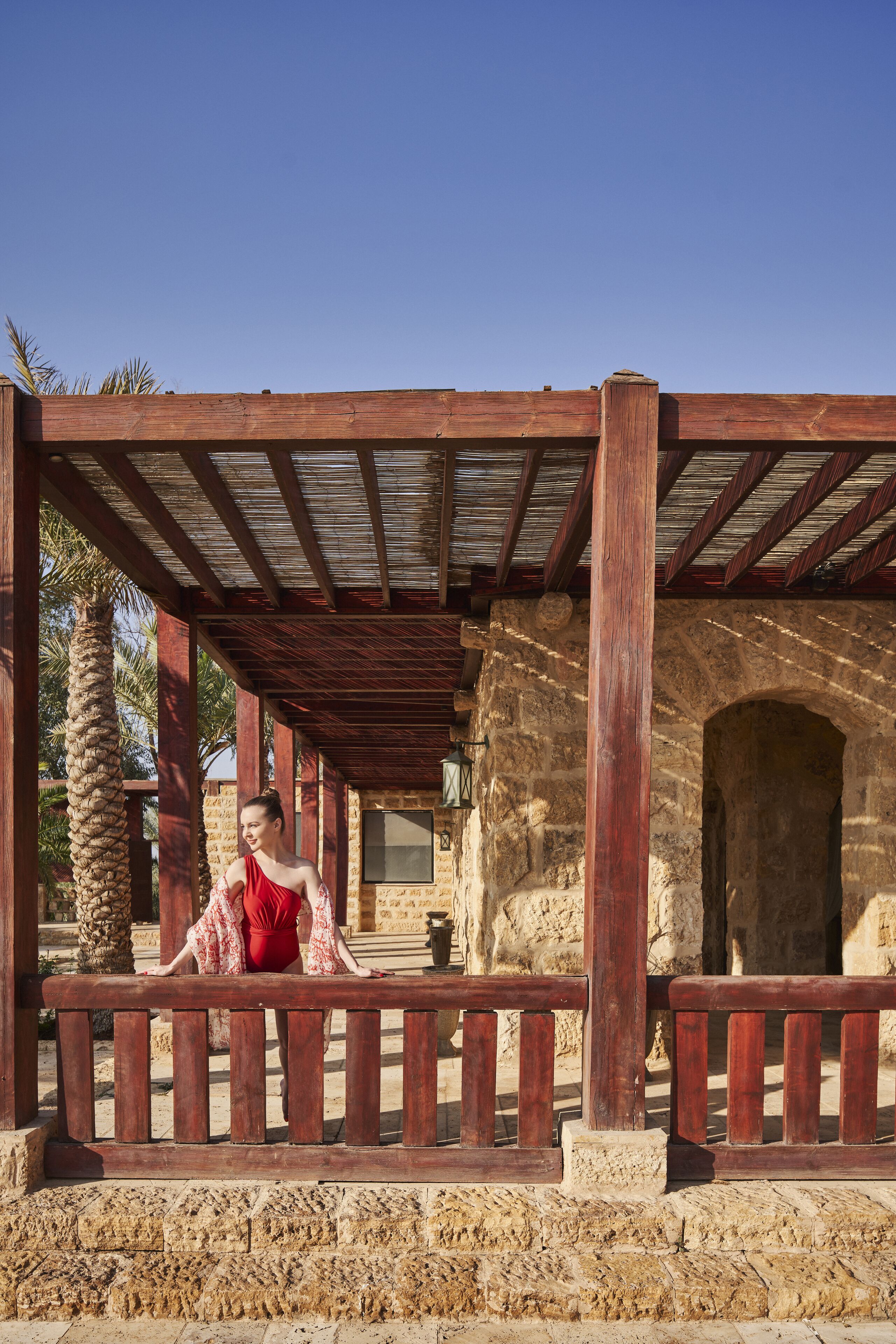 Un espacio al aire libre cubierto con paredes de piedra y vigas de madera, que incluye un arco de piedra y una palmera.