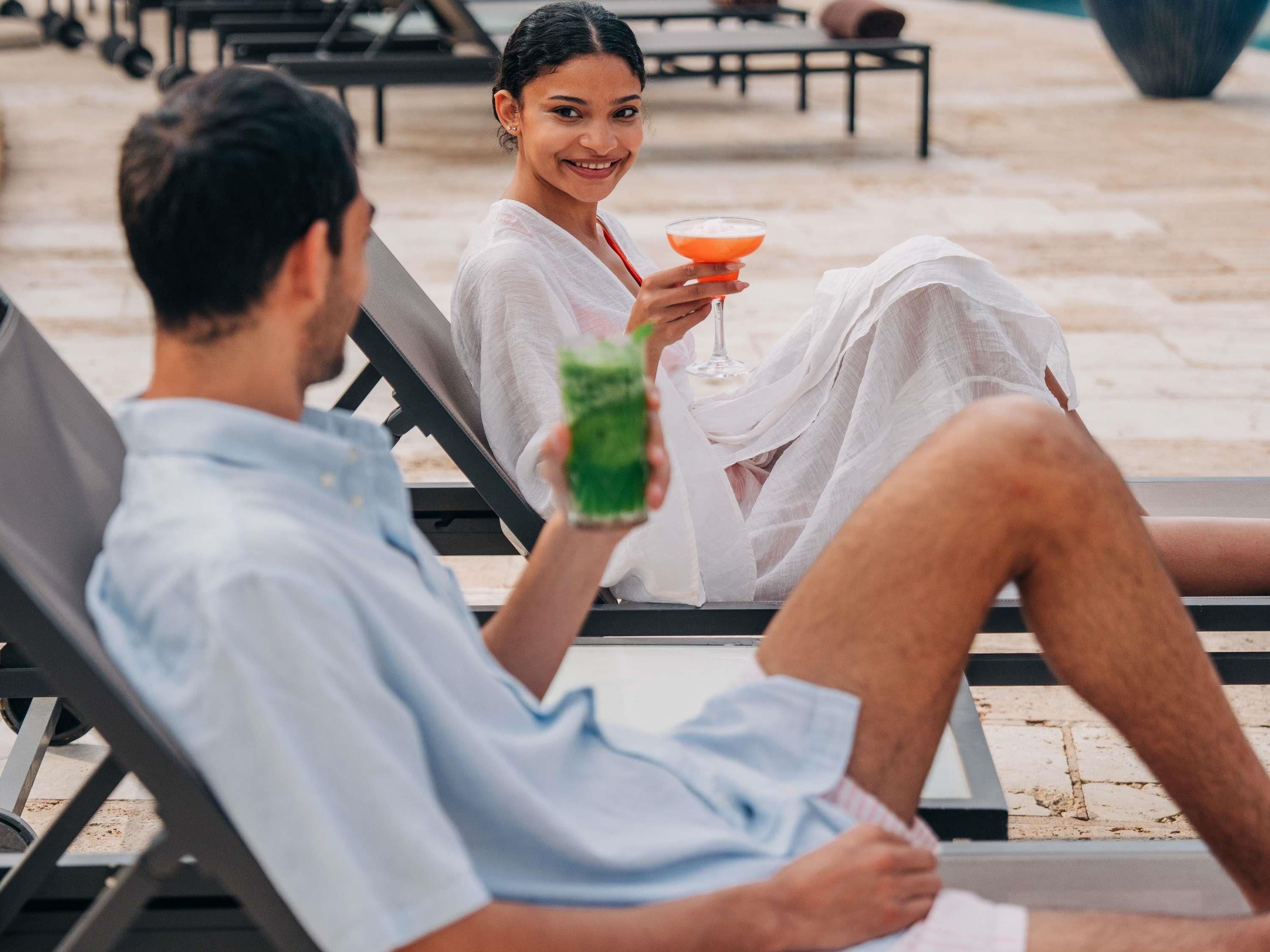 Twee personen leunen achterover op ligstoelen, één met een cocktailglas.