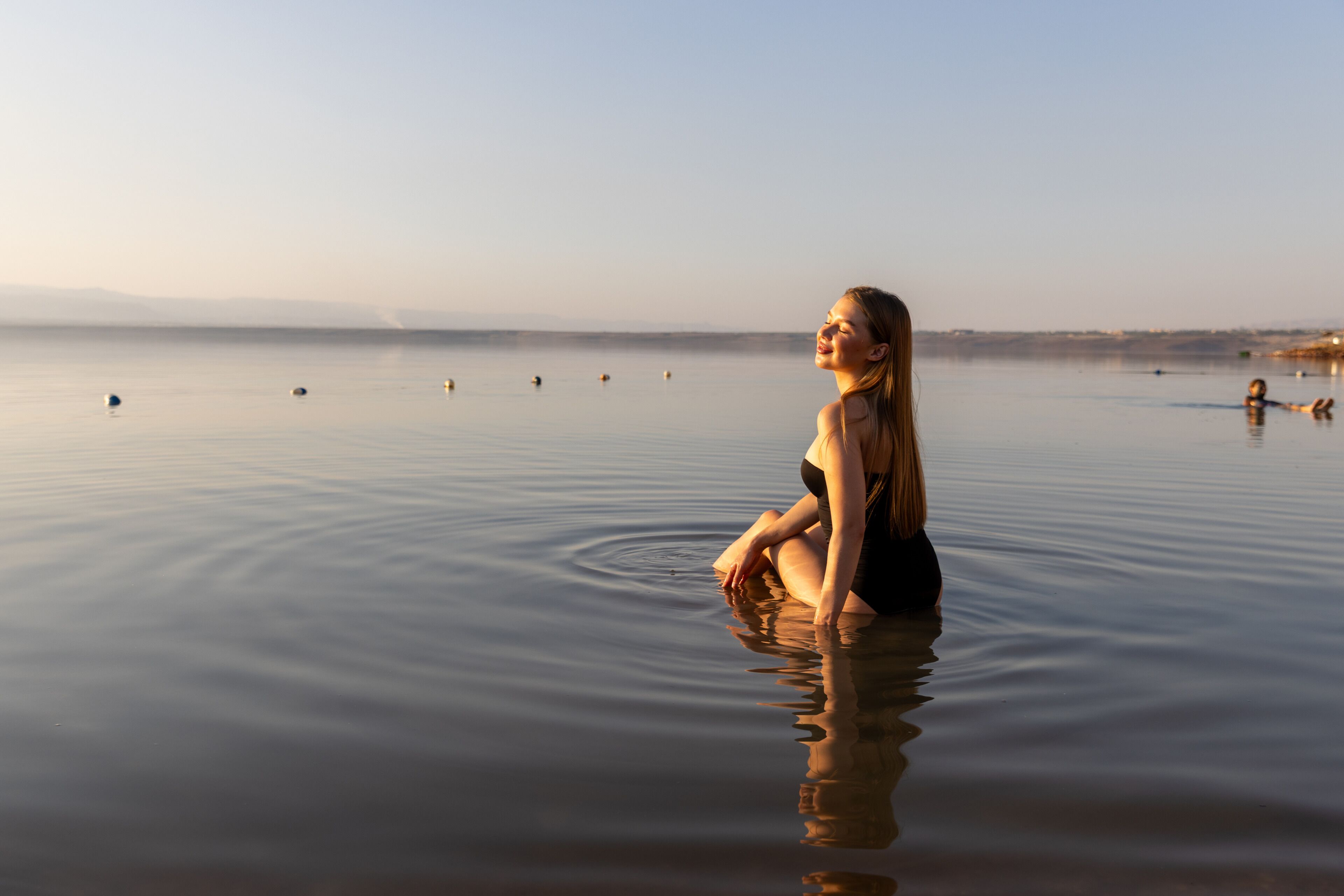 Una mujer sentada en agua tranquila con un cielo despejado al fondo.