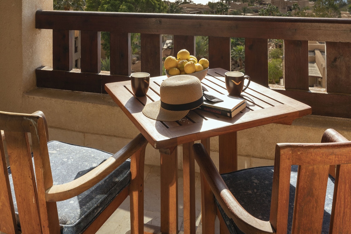 A balcony with a wooden table and chairs, a view of the sea, and a clear sky.