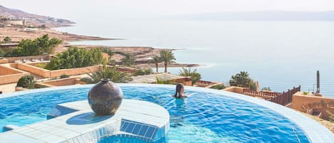 A pool with a view of the sea, a large vase, and a person swimming.