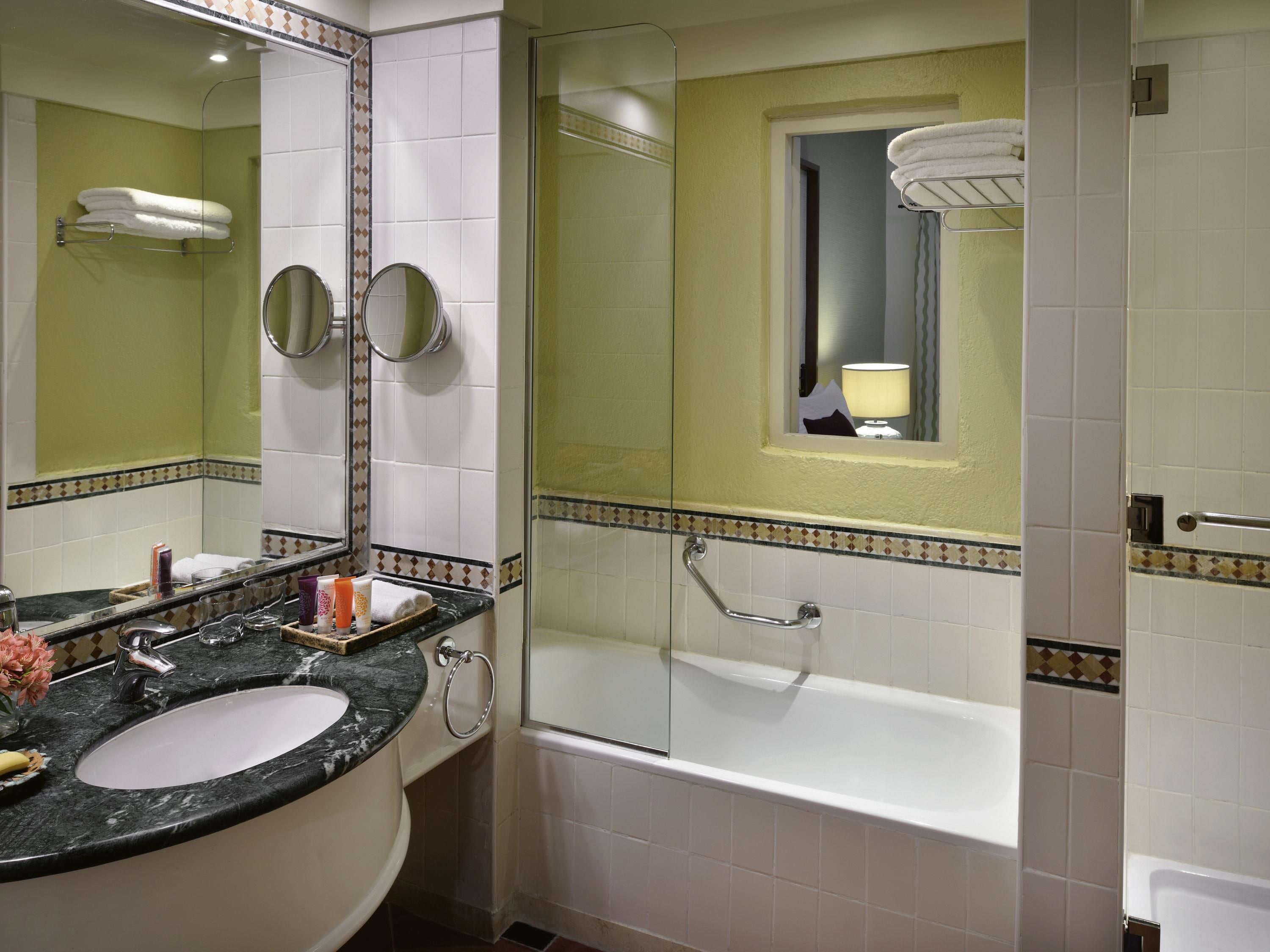 A bathroom with a bathtub, a sink, a mirror, and a window.