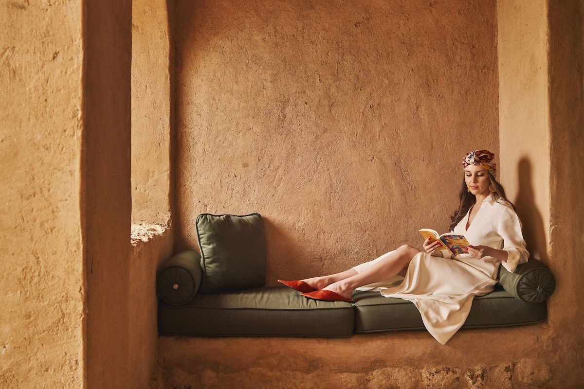 A woman sitting on a green sofa in a room with a textured wall and a hanging light fixture.