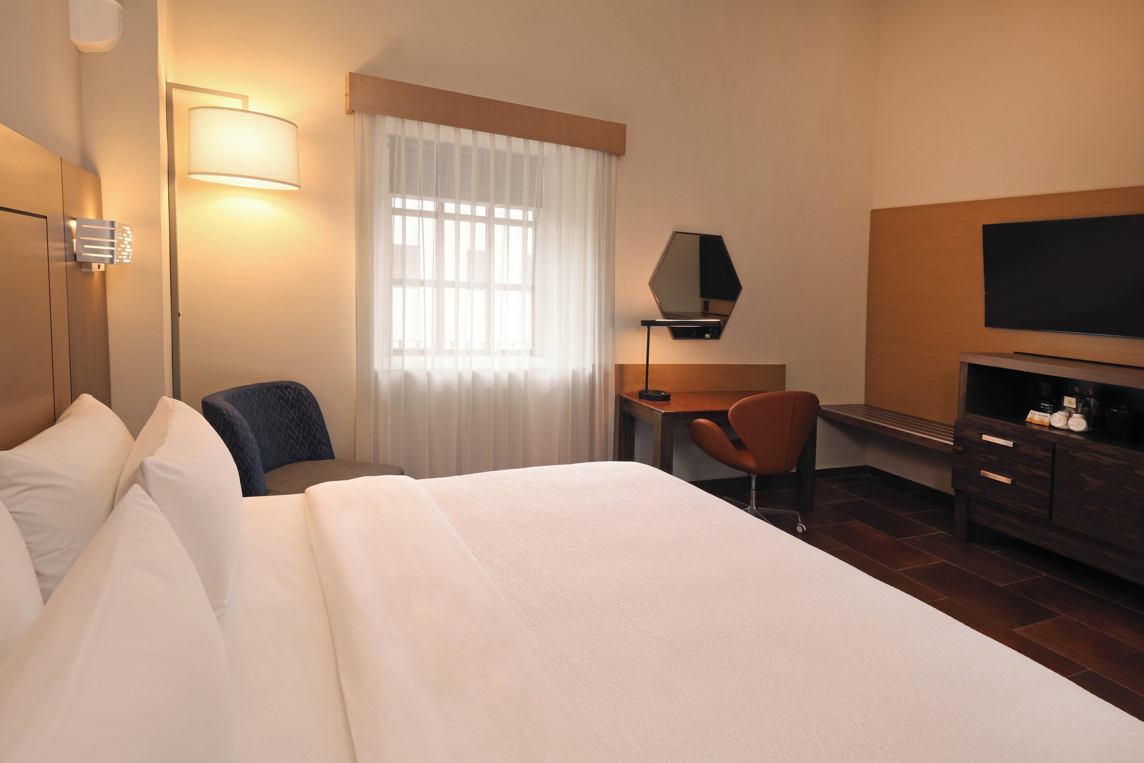 Quarto de hotel com uma cama grande, uma escrivaninha com cadeira, televisão e máquina de café.