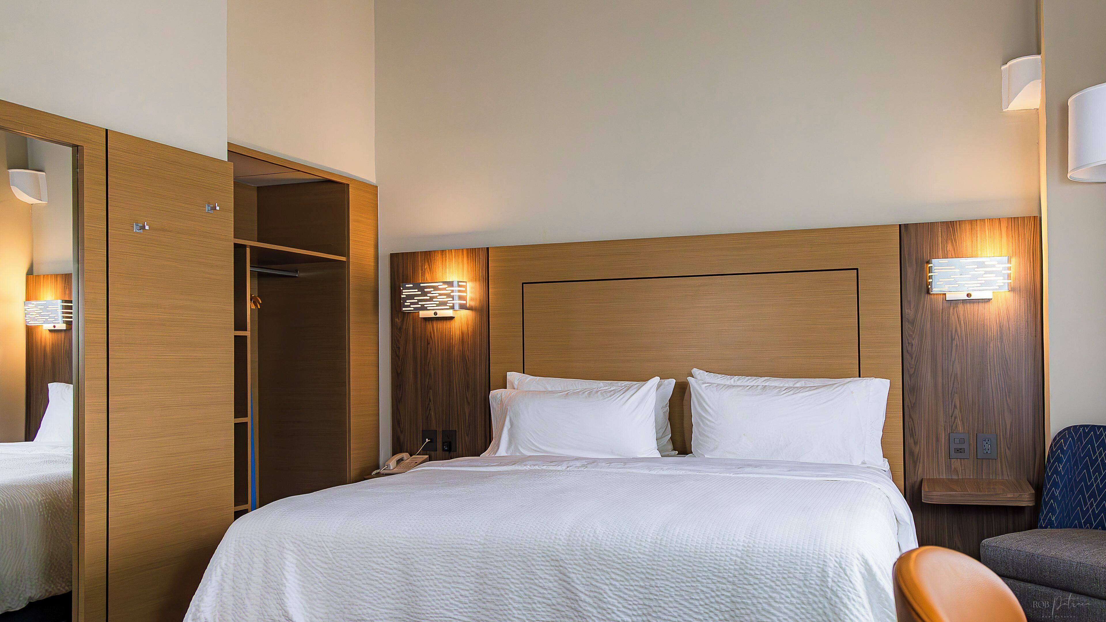 A hotel room with a large bed, a wardrobe, bedside lamps, and a chair.