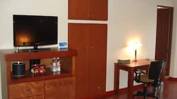 Een kamer met een televisie op een houten kast, een bureau met een stoel en een deur.