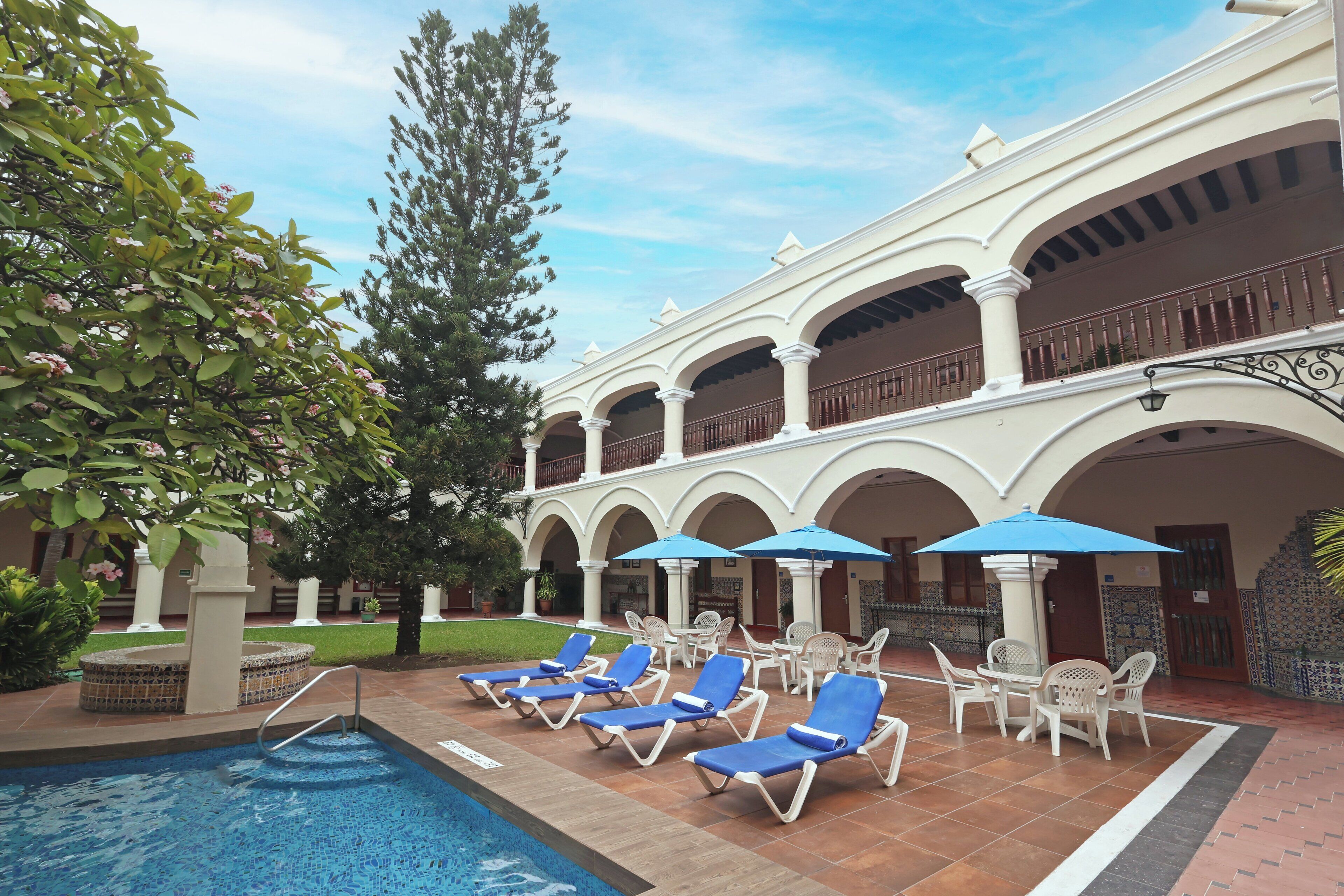 A poolside area with lounge chairs and umbrellas, surrounded by a building with arches and columns.