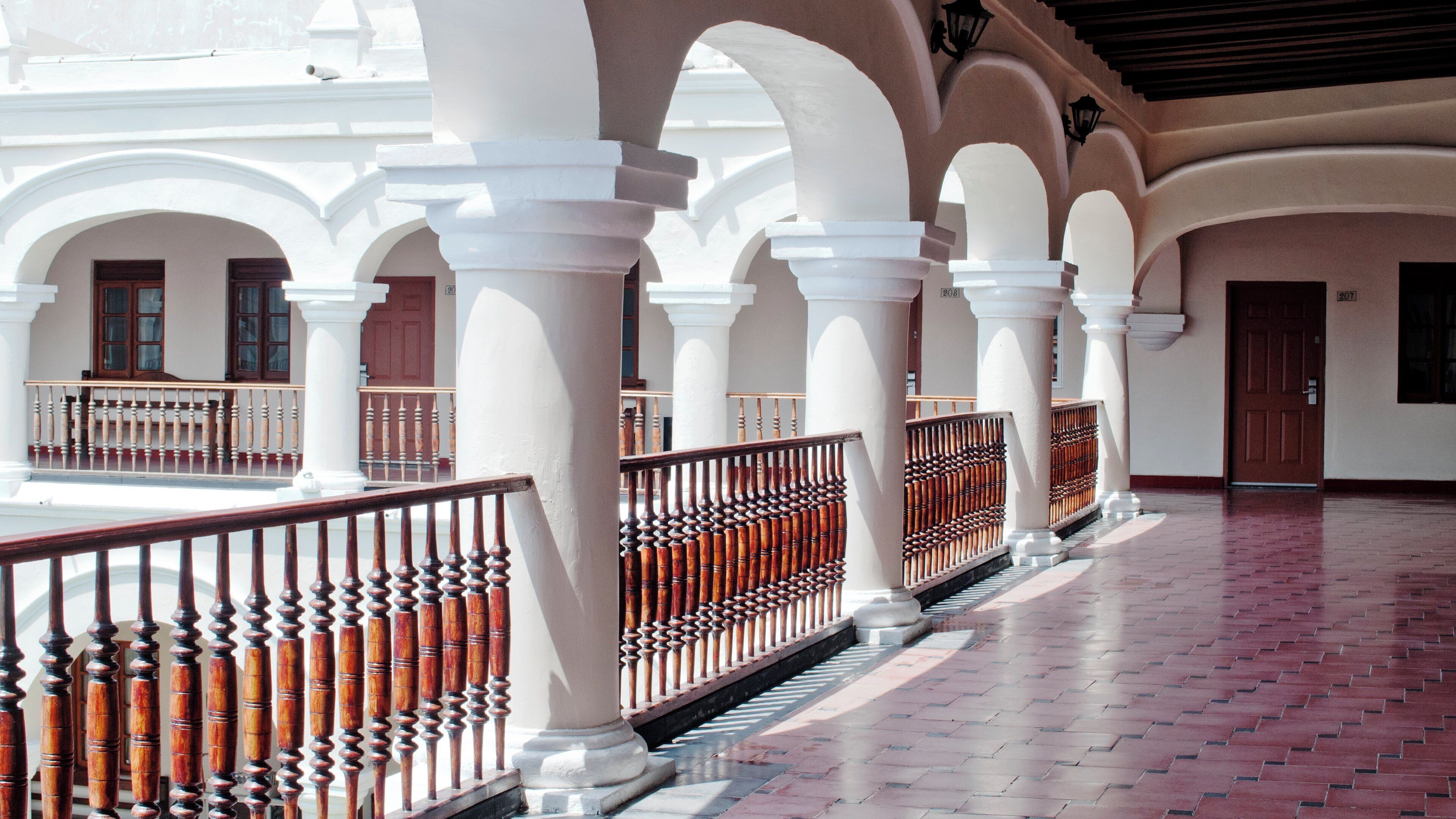 A corridor with white columns, wooden railings, and a tiled floor.