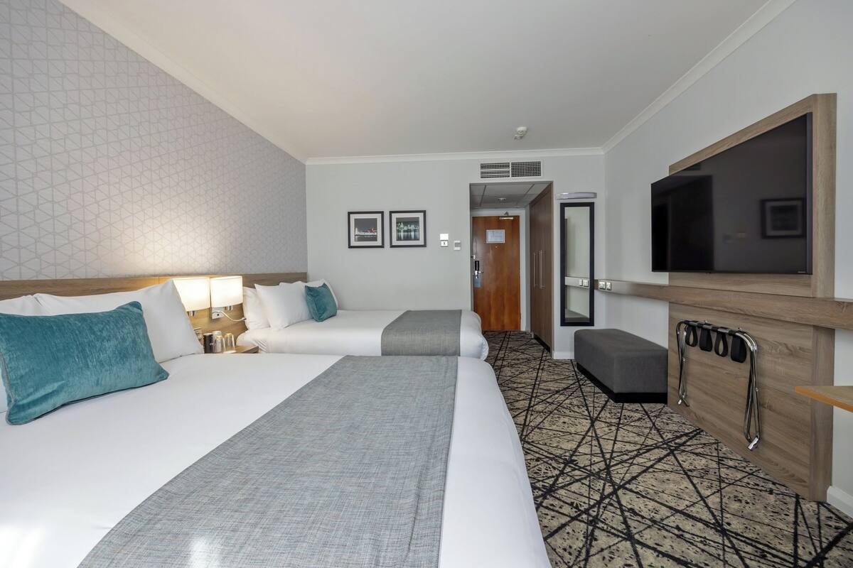 A hotel room with two beds, a TV, a desk, and a patterned carpet.
