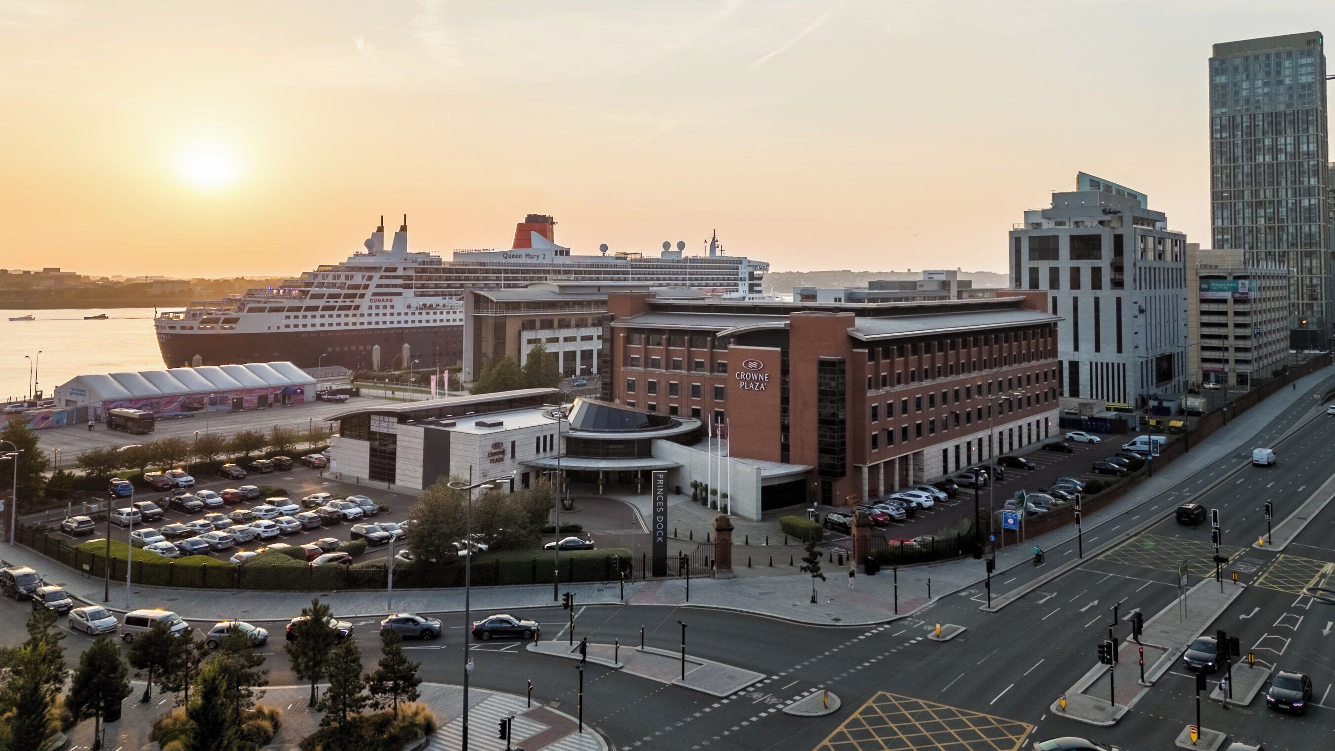 Um cruzeiro atracado num porto com um edifício moderno identificado como "Crowne Plaza" por perto.
