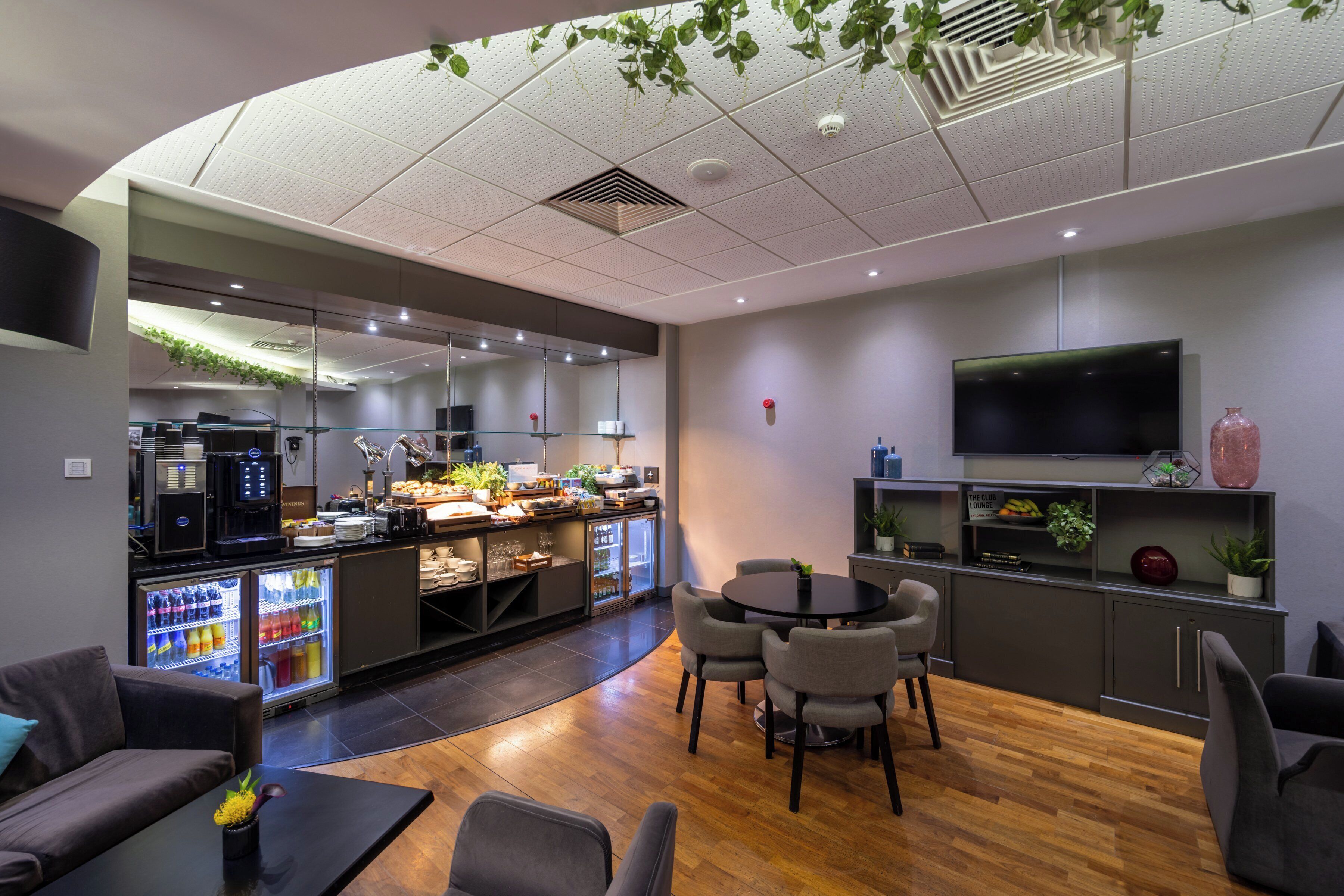 Ett modernt loungeområde med en kaffestation, sittplatser och en tv.