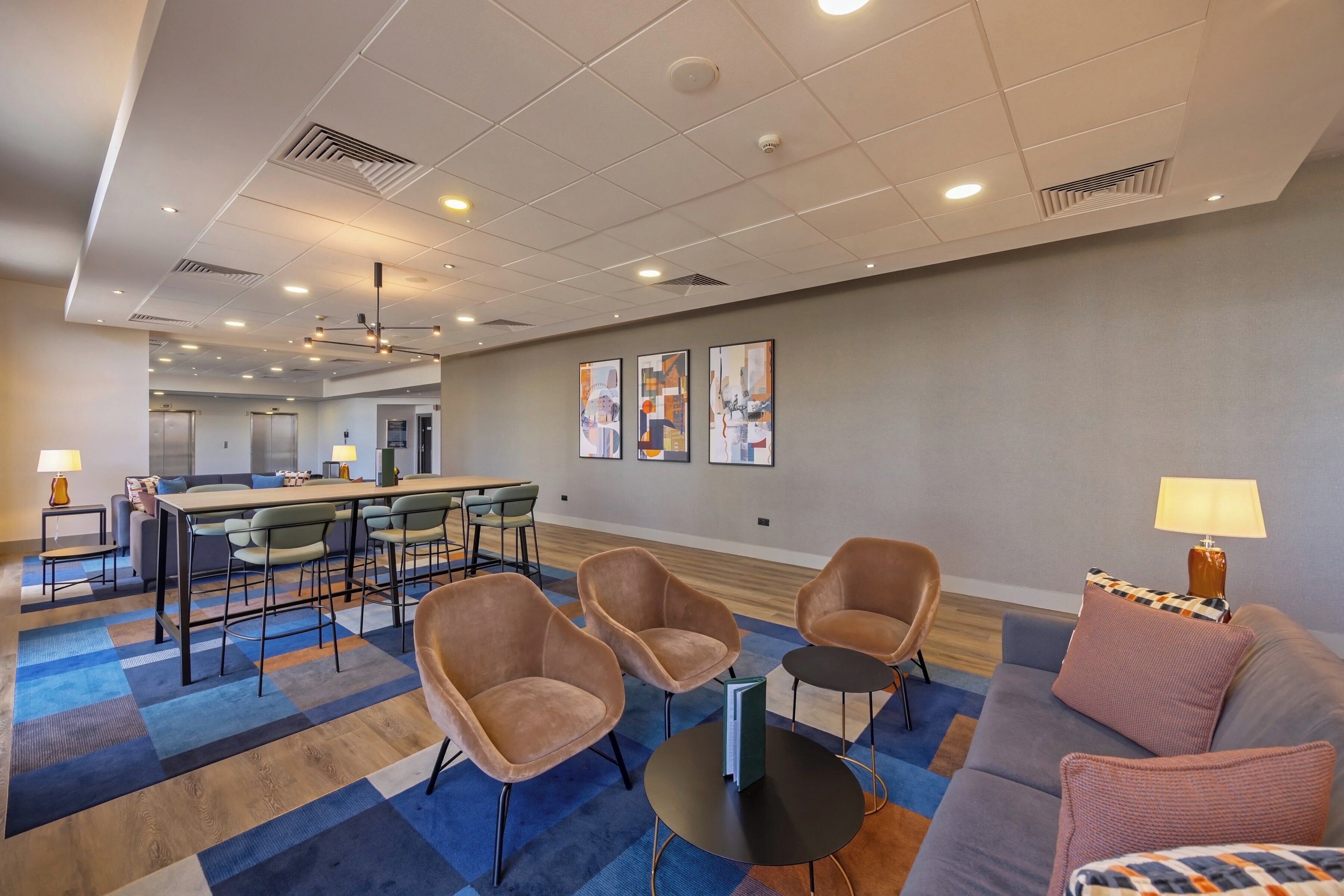 A modern hotel lobby with a seating area, a dining table, and artwork on the walls.