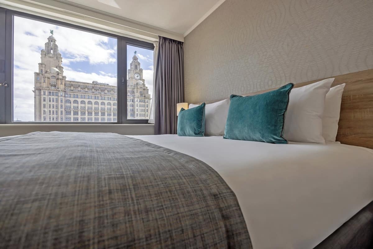 A hotel room with a large bed, a view of a historic building, and a window with curtains.