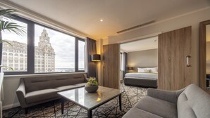 A hotel room with a sofa, armchair, and a small table with a plant. A bed is visible in the background. - Crowne Plaza Liverpool City Centre by IHG (Liverpool)