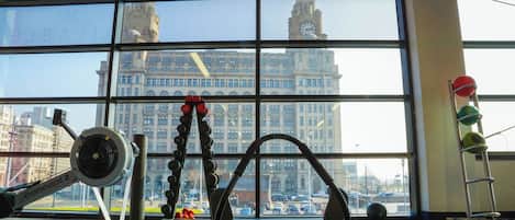 A gym with exercise equipment and a large window overlooking a historic building.