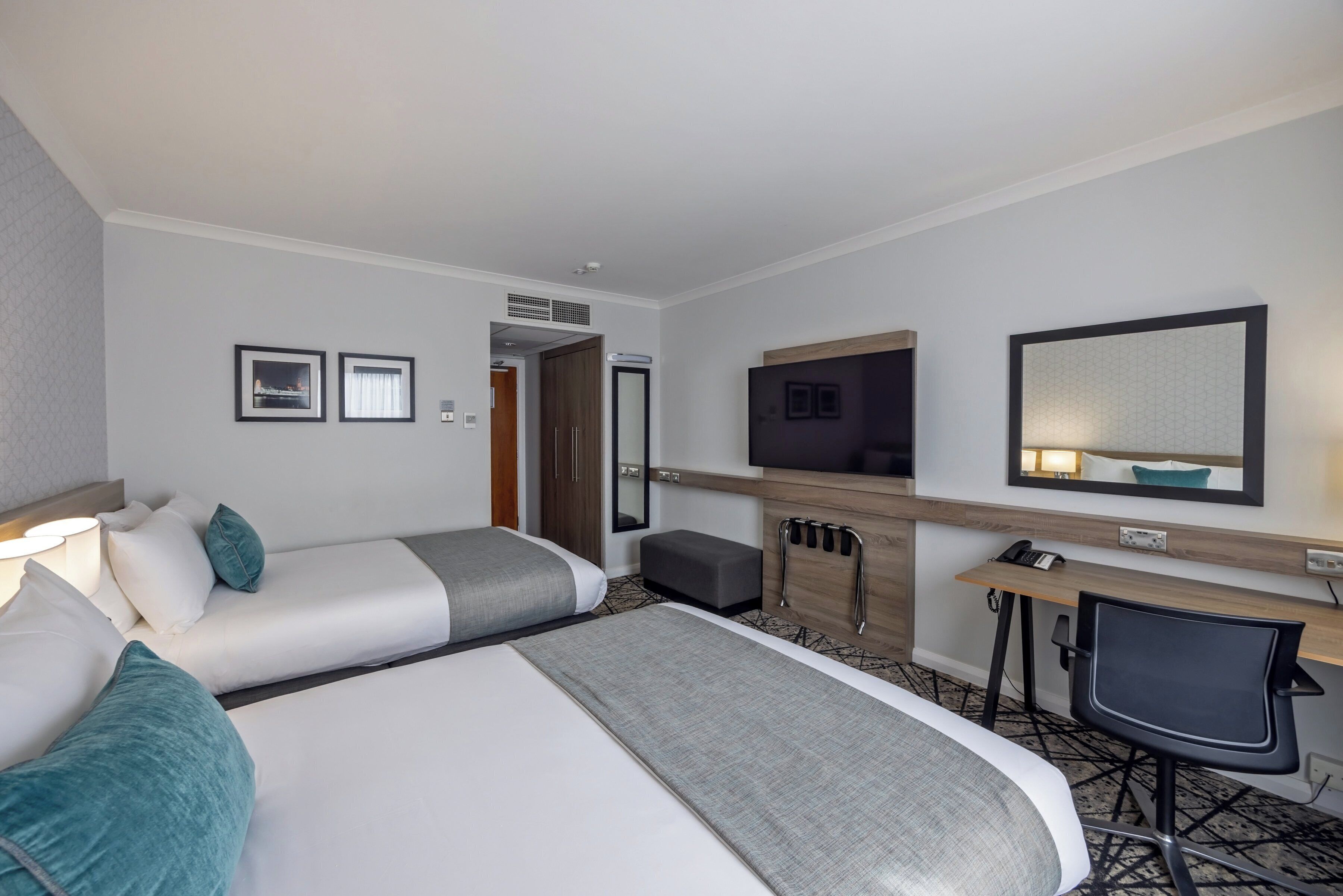 Une chambre d’hôtel équipée d’un lit, d’un bureau, d’une chaise, d’une télévision et d’un miroir.