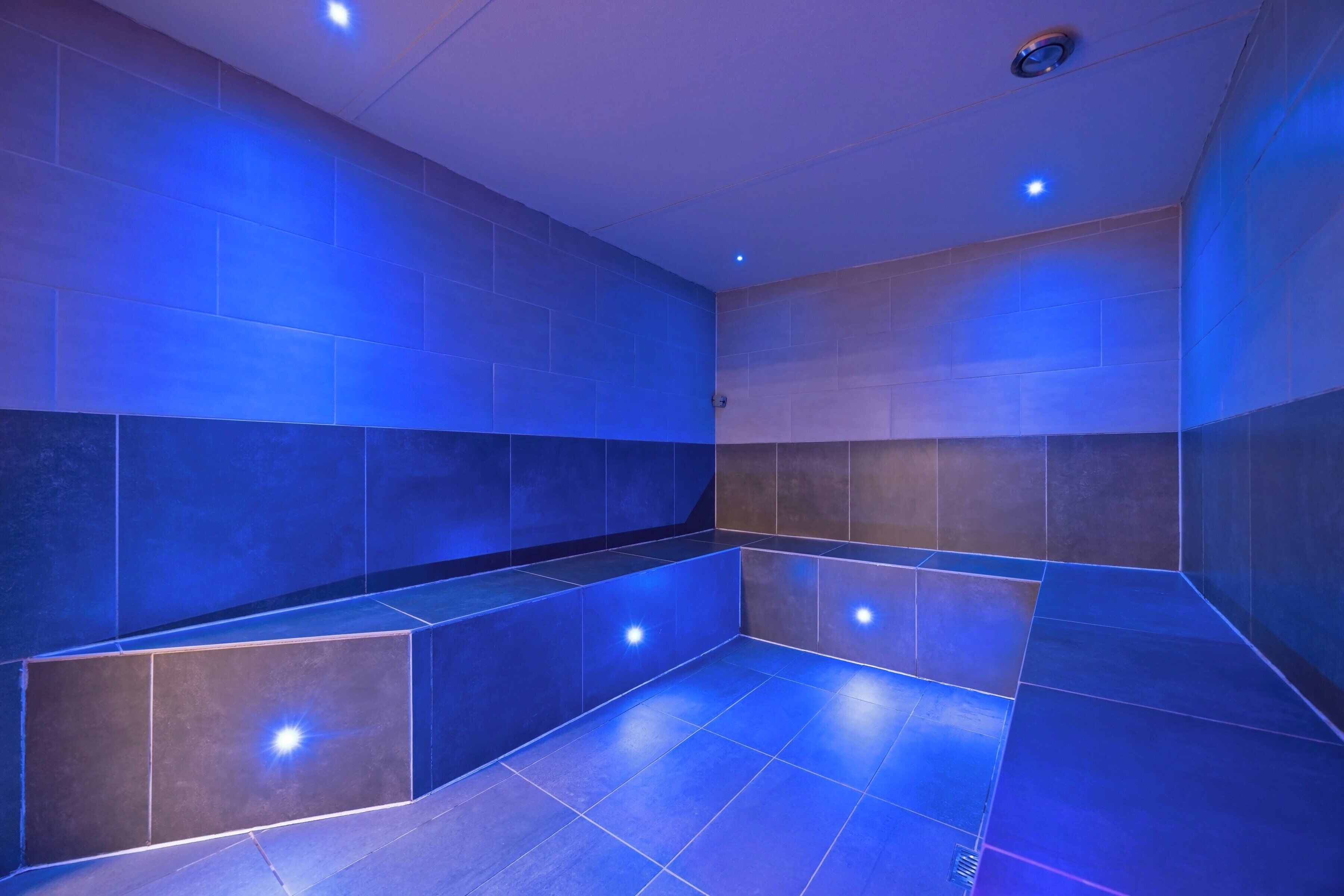 Un baño moderno con iluminación azul, paredes con azulejos y un banco.