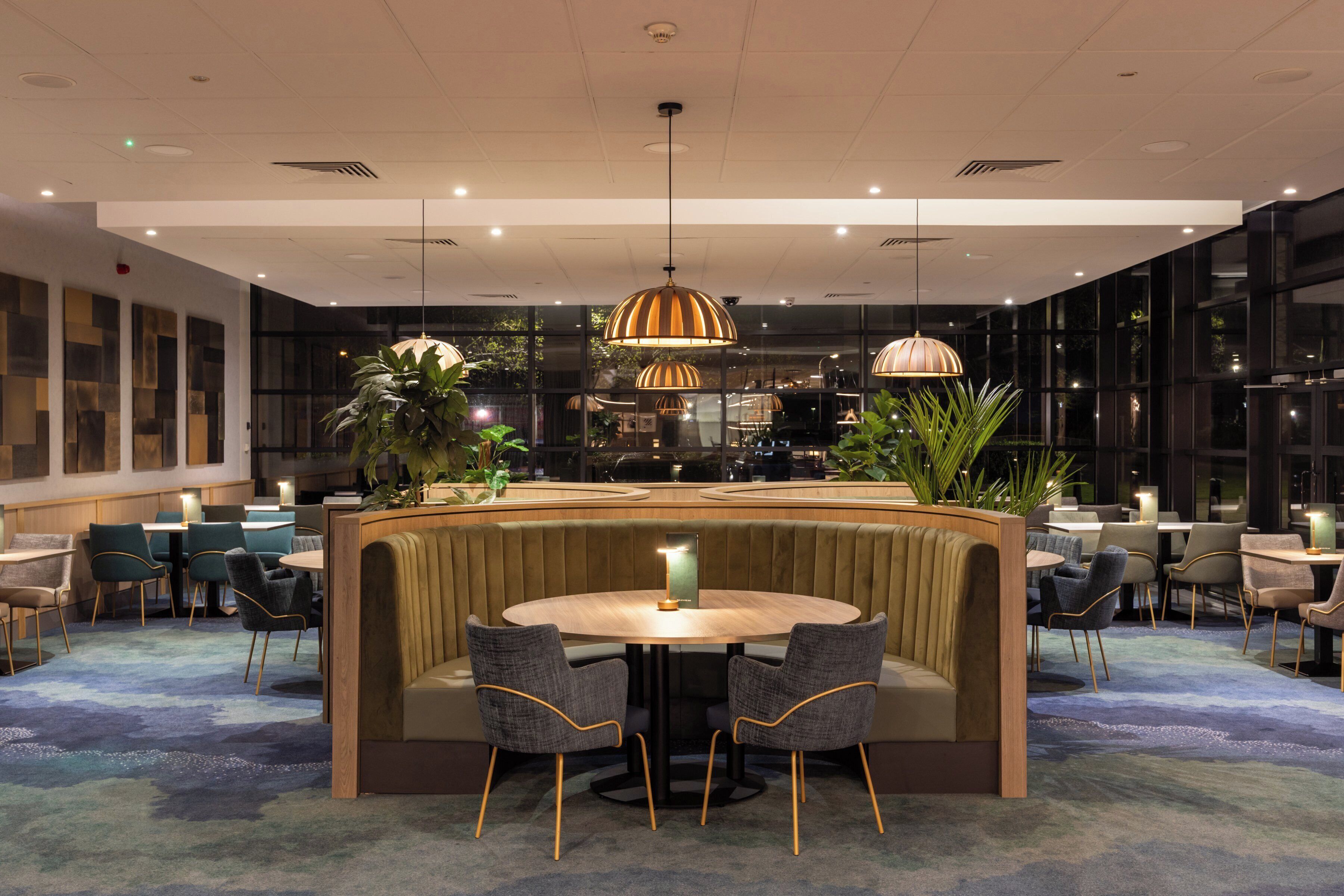 Un moderno hall de hotel con una mesa redonda, zona de estar y grandes ventanales.