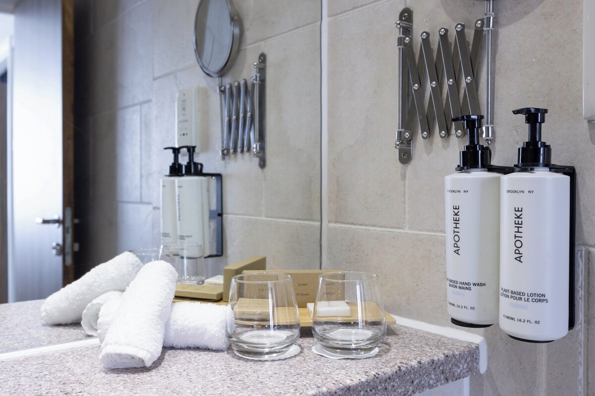 Un baño con encimera de granito, dos botellas de loción, una toalla y un vaso.