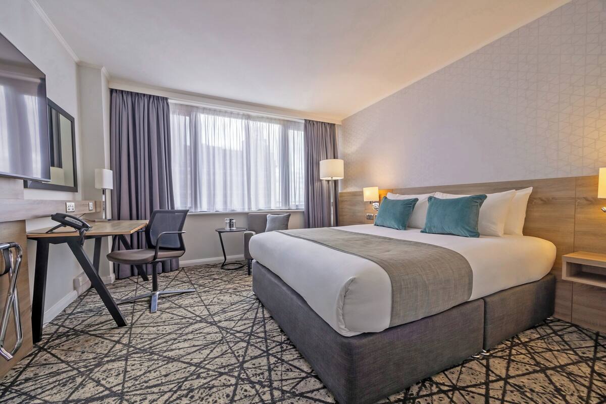 A hotel room with a bed, desk, chair, and a window with curtains.