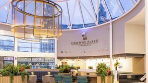 A spacious interior with a high ceiling, a central circular light fixture, seating area with plants, and a reception desk. - Crowne Plaza Liverpool City Centre by IHG (Liverpool)