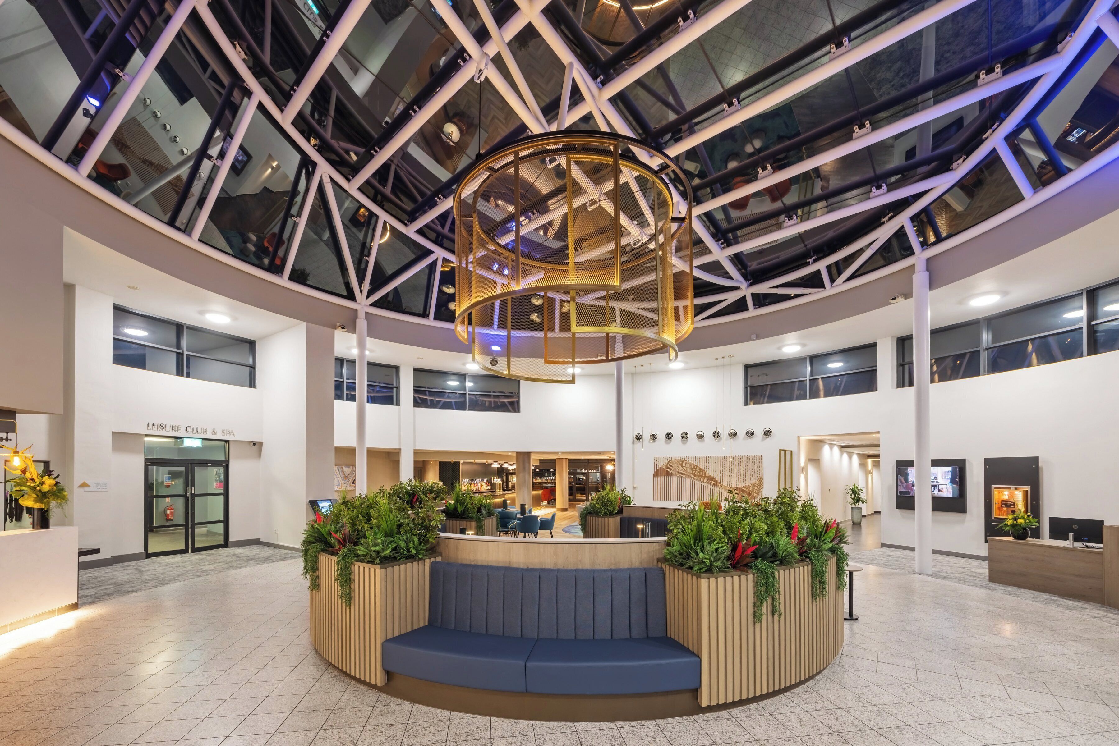 A spacious lobby with a central seating area, a reception desk, and a high ceiling with a geometric glass structure.