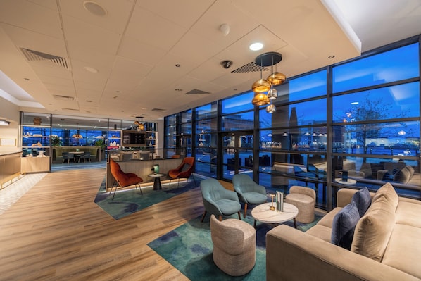 A modern lounge area with seating, a bar, and large windows offering a city view.