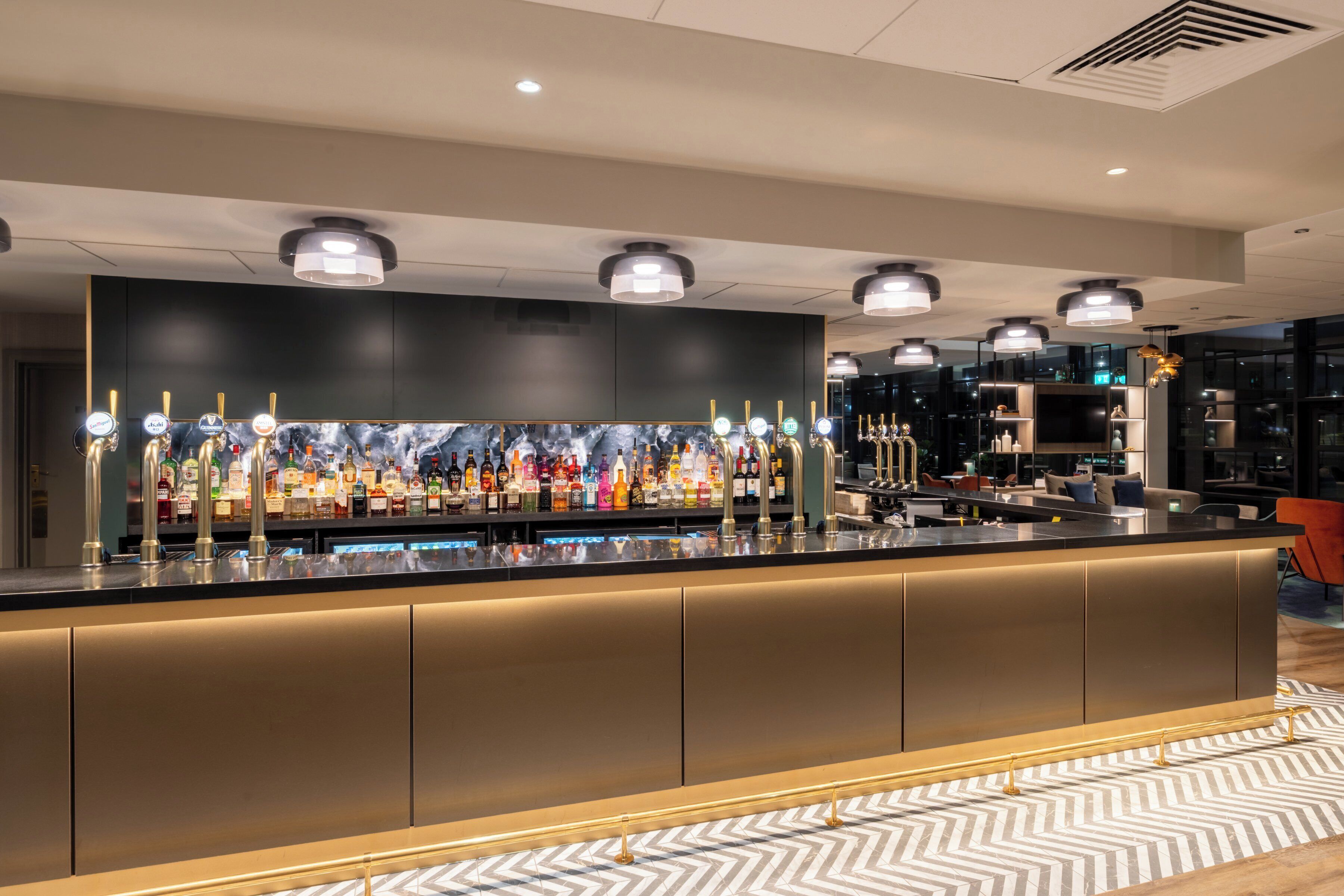 A bar area with a long counter, multiple bottle dispensers, and overhead lighting.