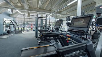 A modern gym with treadmills, weight machines, and a large window offering a view of the city.