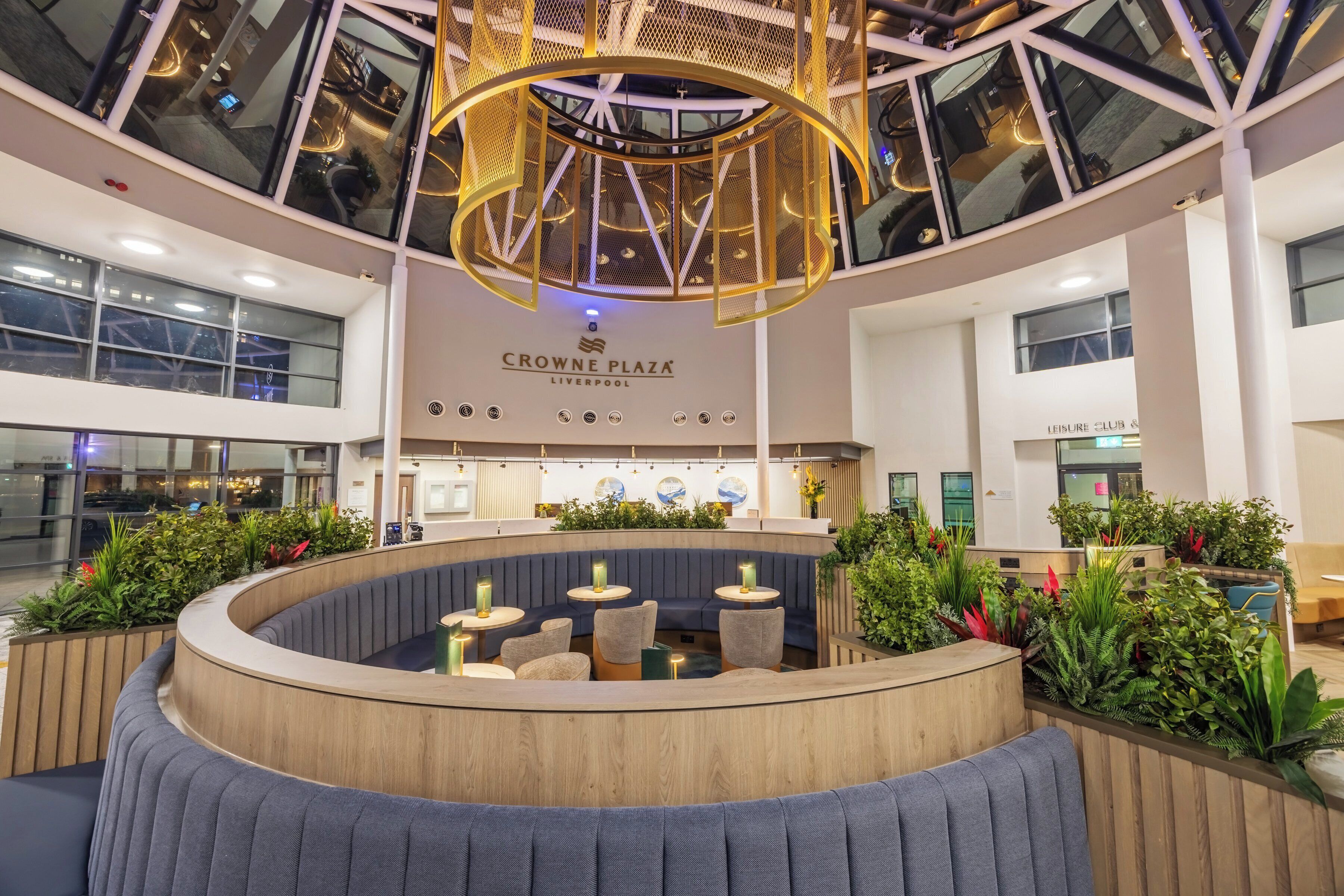A spacious indoor area with a central seating area, a ceiling with a circular light fixture, and a sign for 'Crowne Plaza Liverpool.'