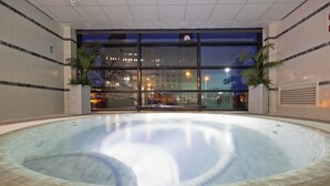 Una piscina interior con borde de azulejos, ventanas amplias y dos plantas en macetas.