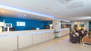 A hotel reception area with a blue wall, a reception desk, a clock, and a seating area with sofas and a table. - Holiday Inn Express Taunton East by IHG (Taunton)