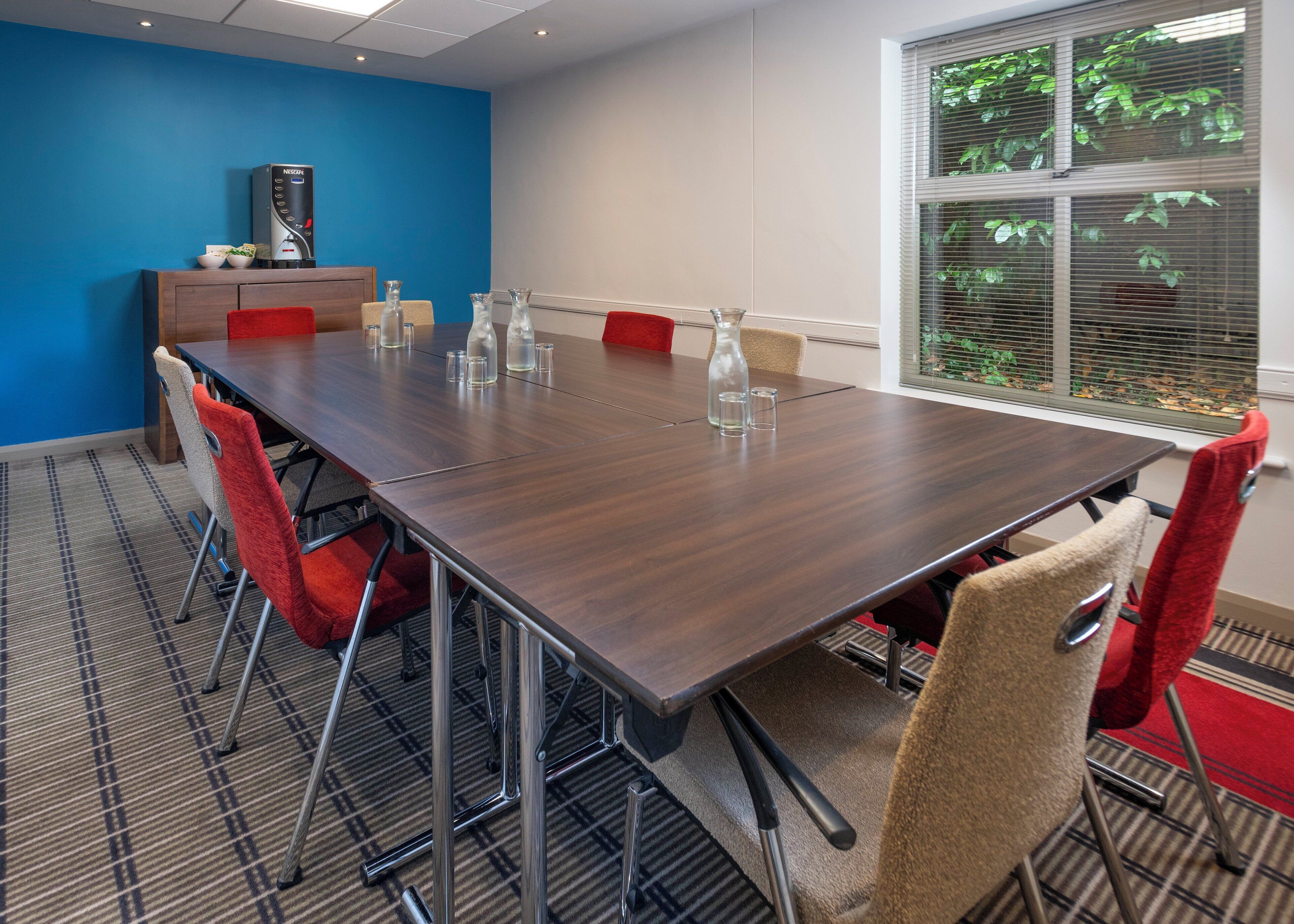 A conference room with a long table, red chairs, and a coffee machine.