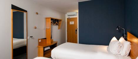 A hotel room with two beds, a wooden dresser, a mirror, a coat rack, and an air conditioning unit.