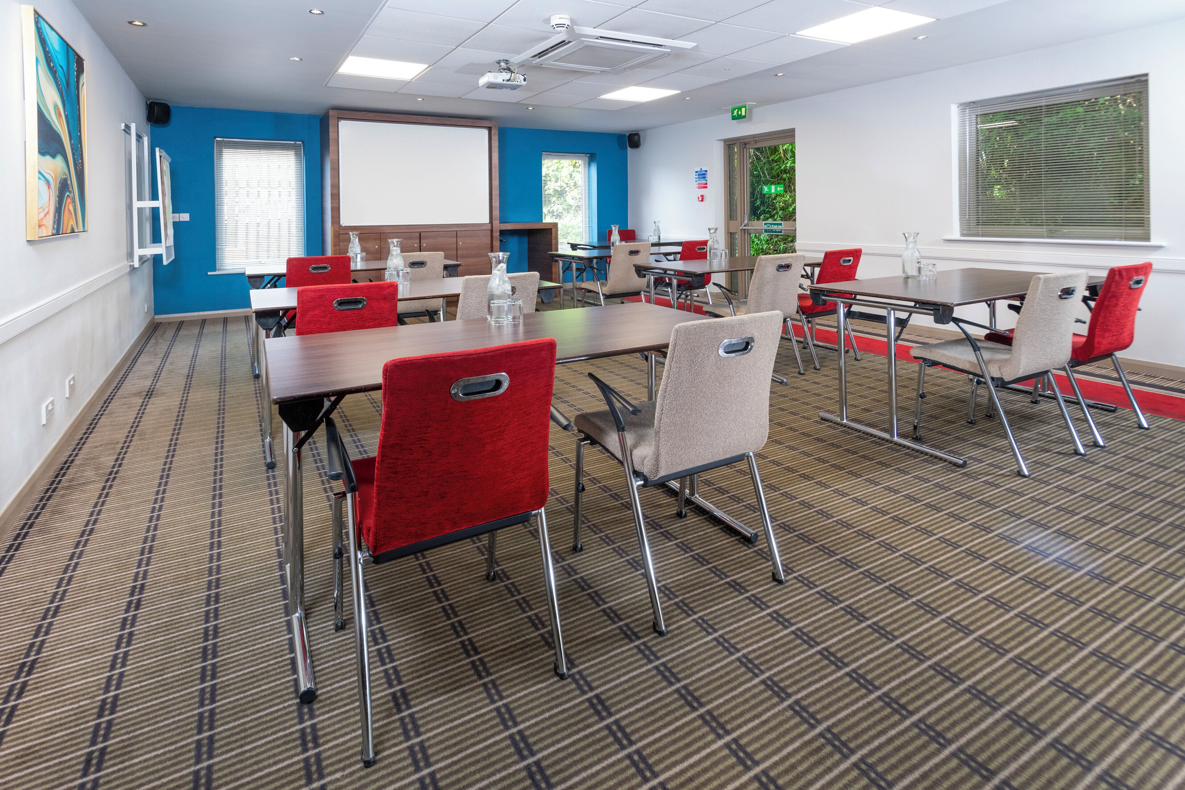 A conference room with tables, chairs, a projector screen, and a whiteboard.