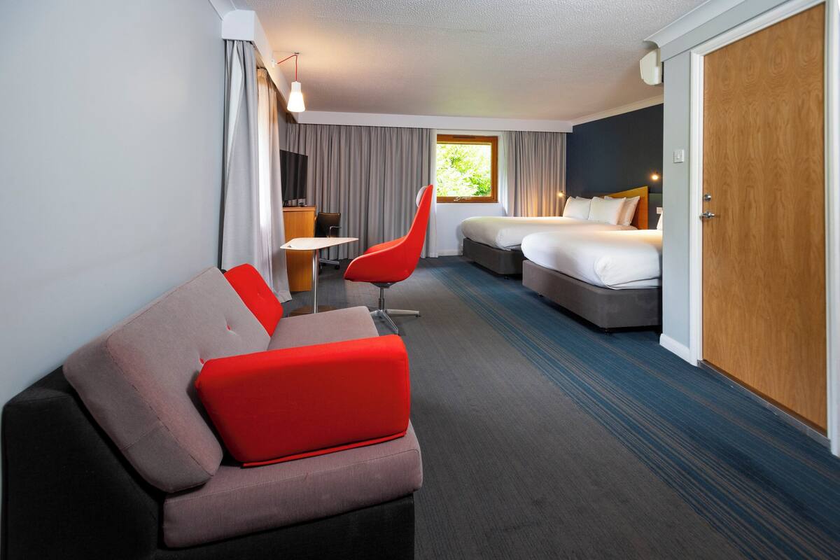 A hotel room with a bed, a sofa, a chair, a desk, and a wardrobe.