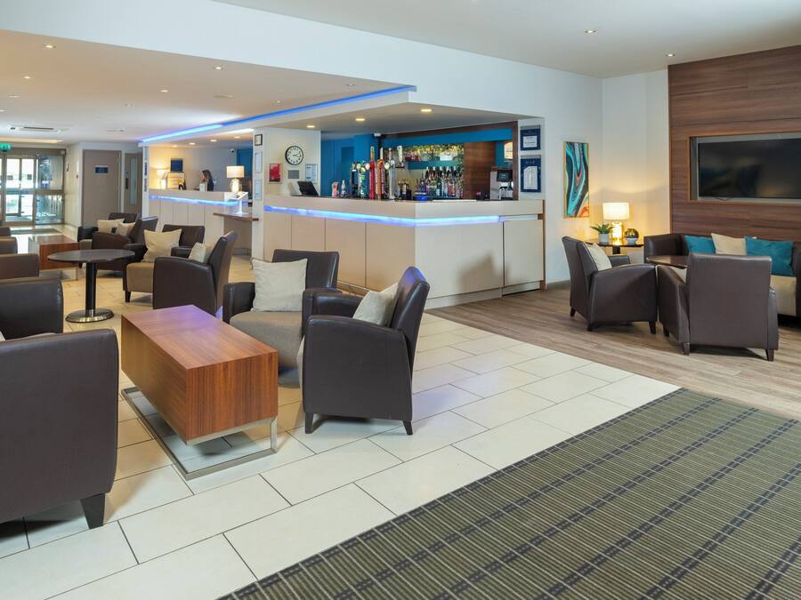 Un vestíbulo moderno con zona de bar, asientos y mostrador de recepción.