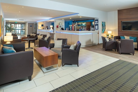 A modern lobby with a bar area, seating arrangements, and a reception desk.