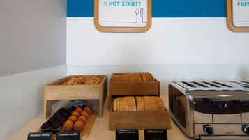 Un présentoir de petit-déjeuner avec divers muffins et pains, un grille-pain et des panneaux d’information indiquant la teneur en calories.