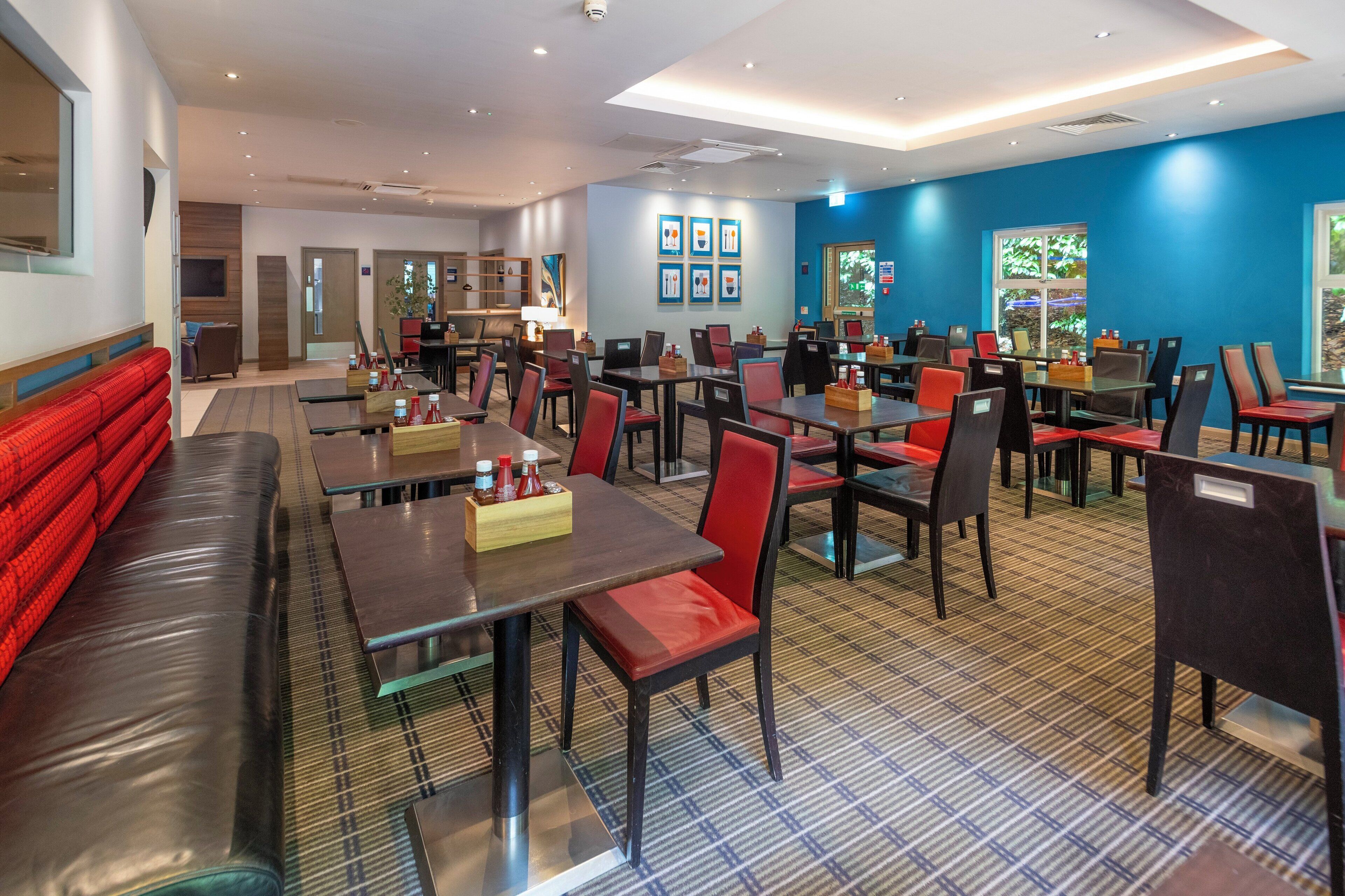 A modern restaurant with multiple dining areas, including booths and tables with red chairs.