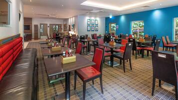 A modern restaurant with multiple dining areas, including booths and tables with red chairs.