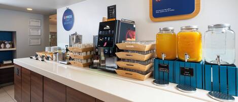 A breakfast bar with a coffee machine, juice dispensers, and a sign encouraging guests to wake up and have breakfast.