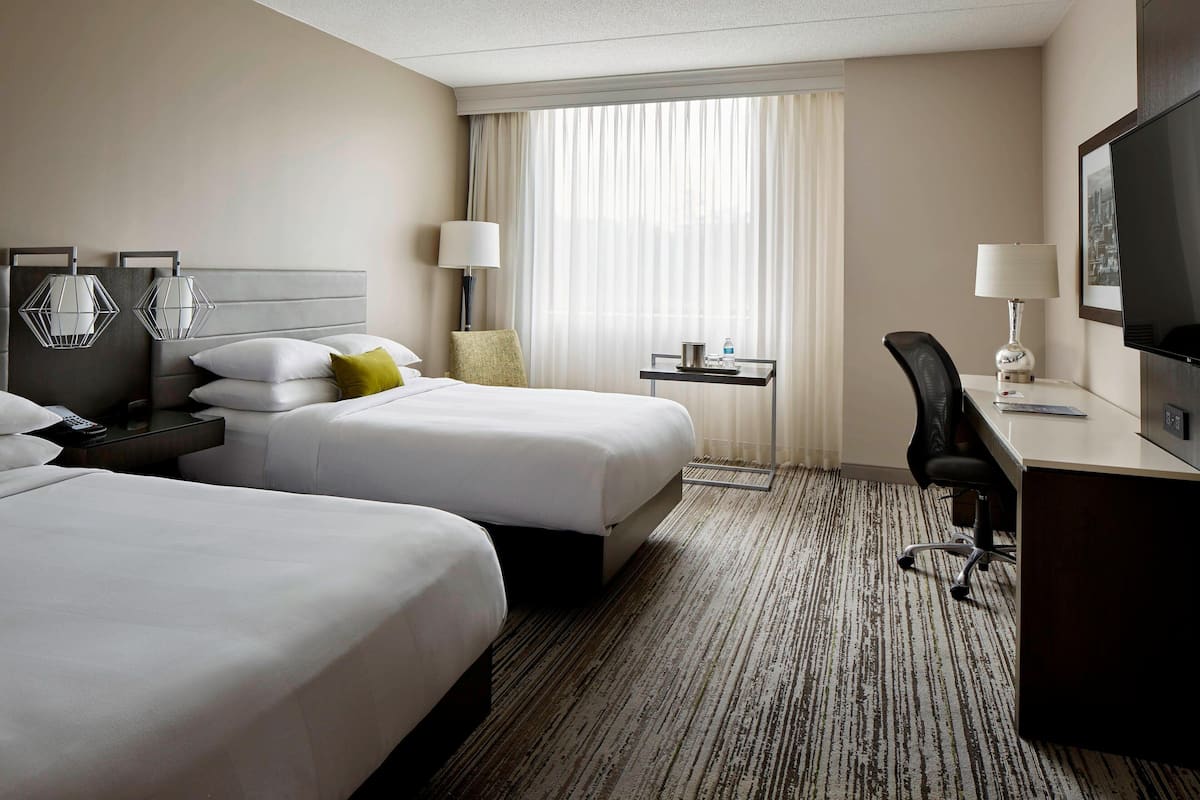 Habitación de hotel con dos camas, un escritorio, una silla, un televisor y una ventana con cortinas.